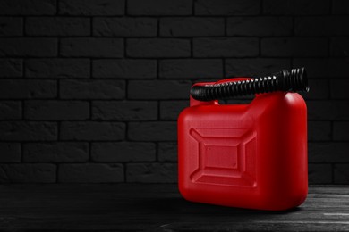 Photo of Red plastic canister on black wooden table against dark brick wall, space for text