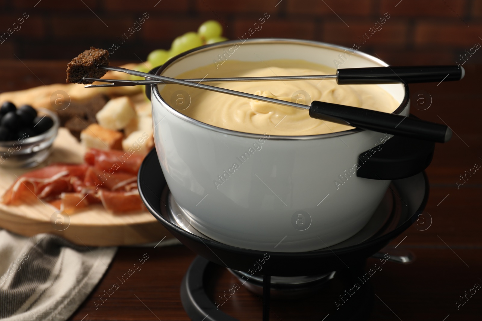 Photo of Fondue with tasty melted cheese, forks and piece of bread on wooden table