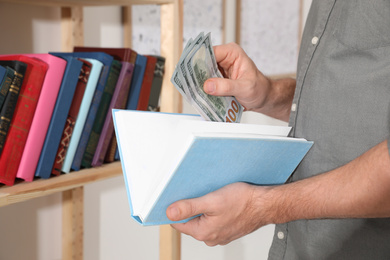 Photo of Man hiding money in book indoors, closeup. Financial savings