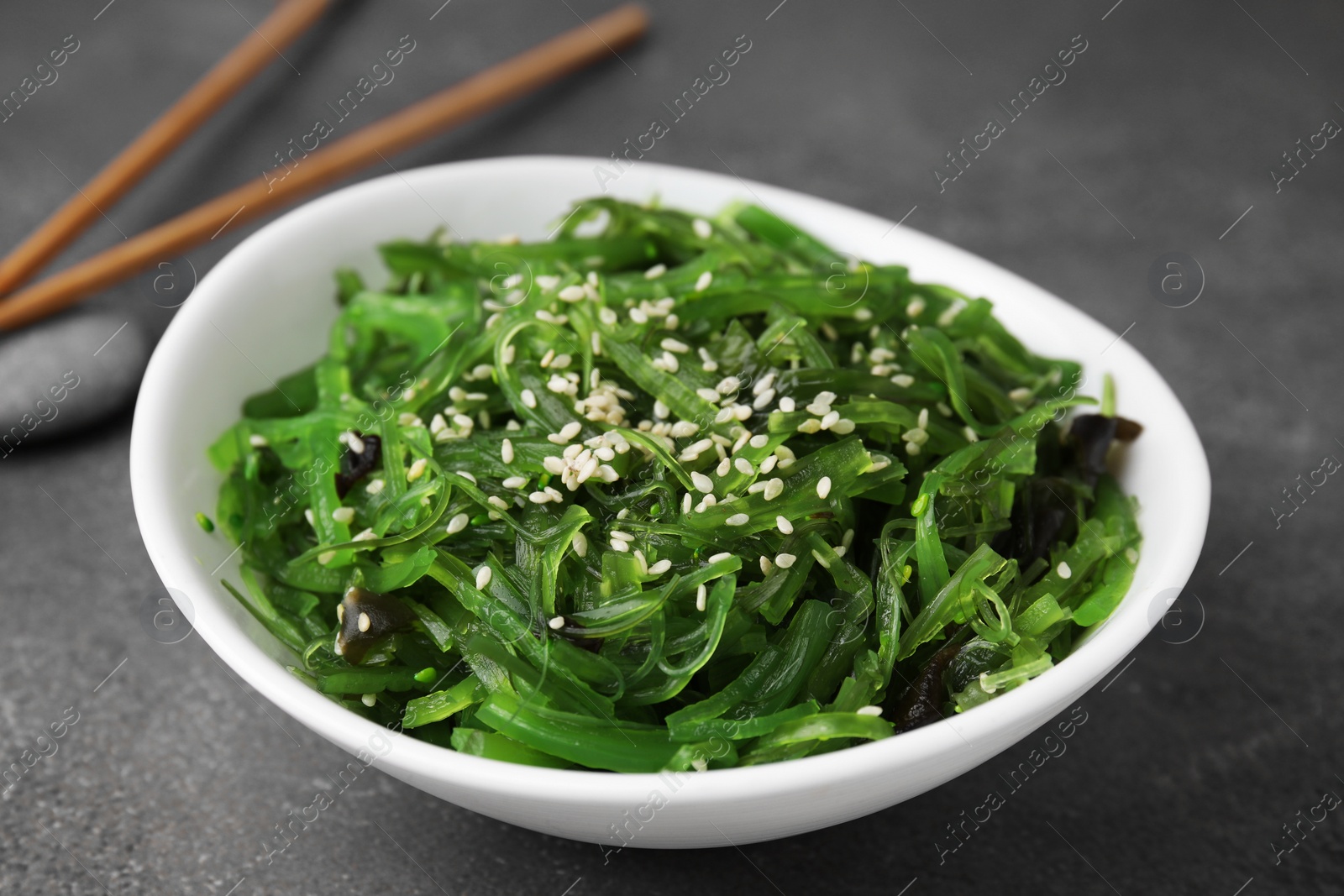 Photo of Tasty seaweed salad in bowl served on brown table, closeup