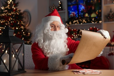 Santa Claus reading letter at table in room decorated for Christmas