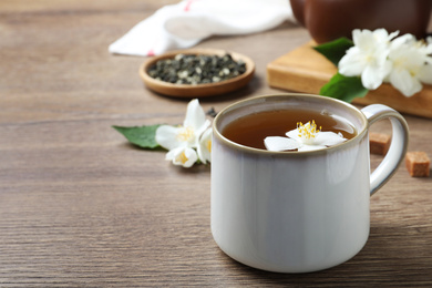 Photo of Cup of tea with fresh jasmine flower on wooden table. Space for text