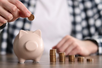 Photo of Financial savings. Man putting coin into piggy bank at wooden table, closeup