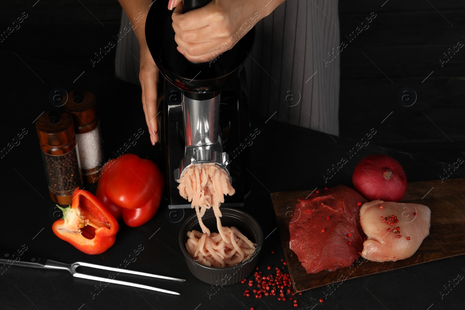 Photo of Woman making chicken mince with electric meat grinder at black table, closeup