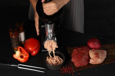 Photo of Woman making chicken mince with electric meat grinder at black table, closeup