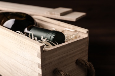 Photo of Open wooden crate with bottle of wine on dark background, closeup