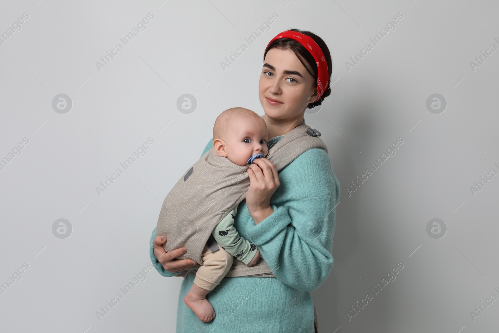 Photo of Mother holding her child in sling (baby carrier) on light grey background