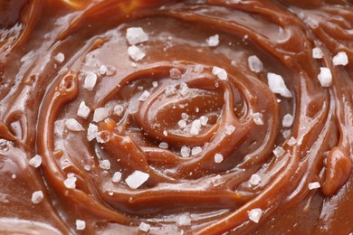 Tasty caramel sauce and salt as background, closeup