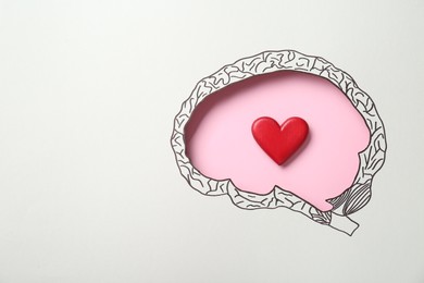 Emotional thinking. Red heart on pink background, top view through paper with brain shaped hole and drawing. Space for text