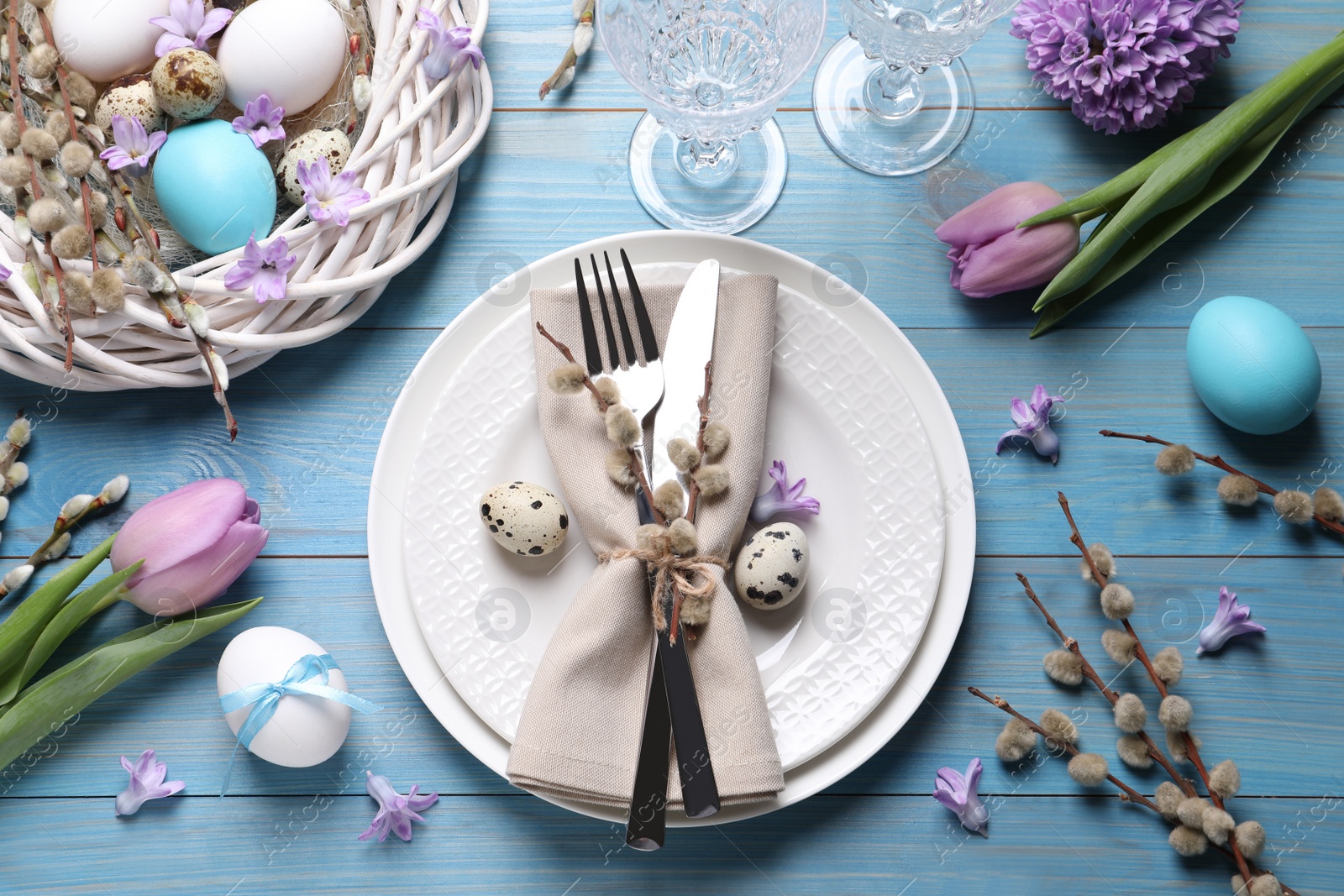 Photo of Festive Easter table setting with painted eggs and floral decor on light blue wooden background, flat lay