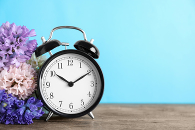 Photo of Black alarm clock and spring flowers on light blue background, space for text. Time change