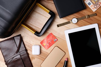 Business trip stuff and suitcase on wooden surface, flat lay