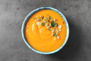 Photo of Delicious pumpkin soup in bowl on grey table, top view