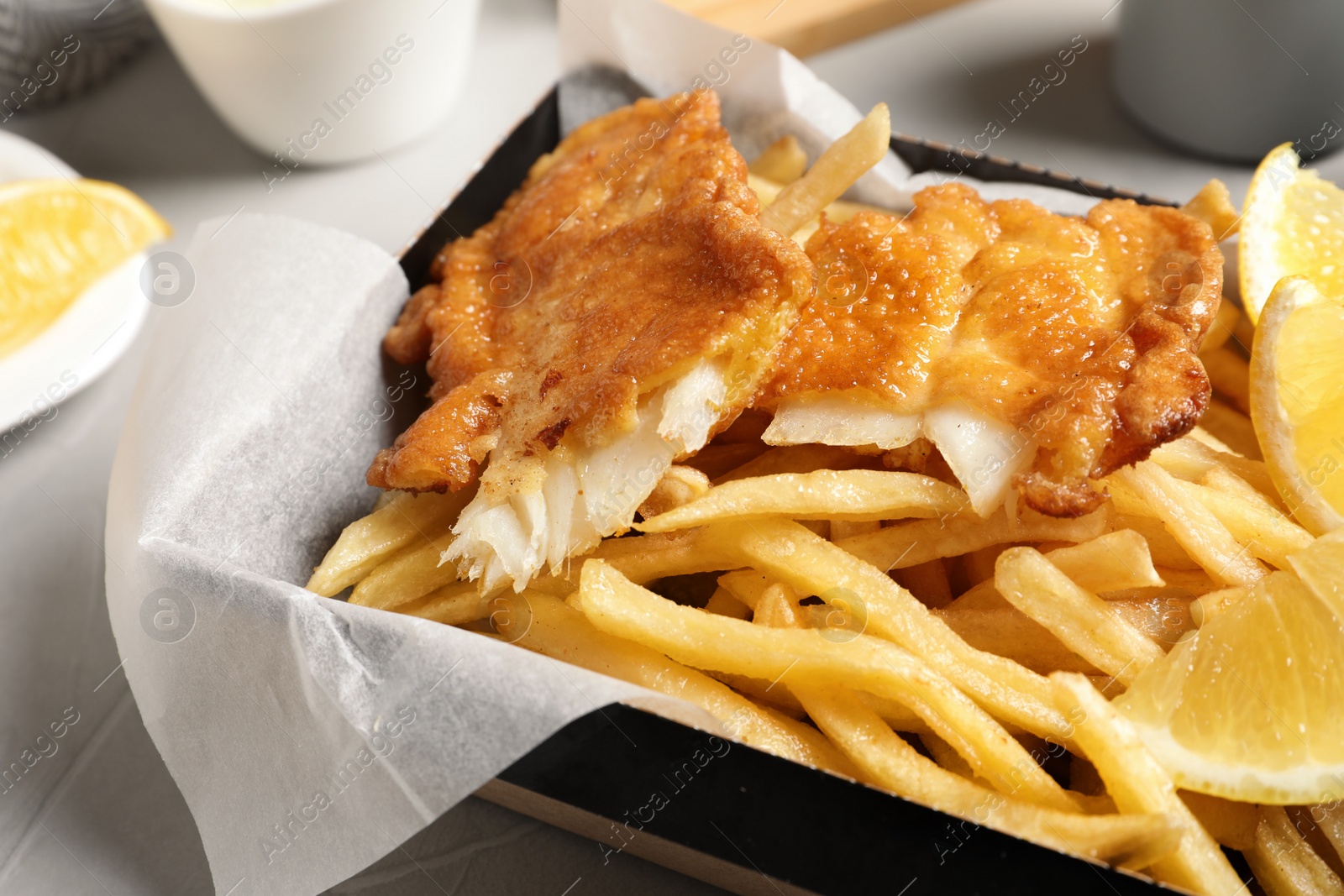 Photo of Container with British traditional fish and potato chips on table, closeup