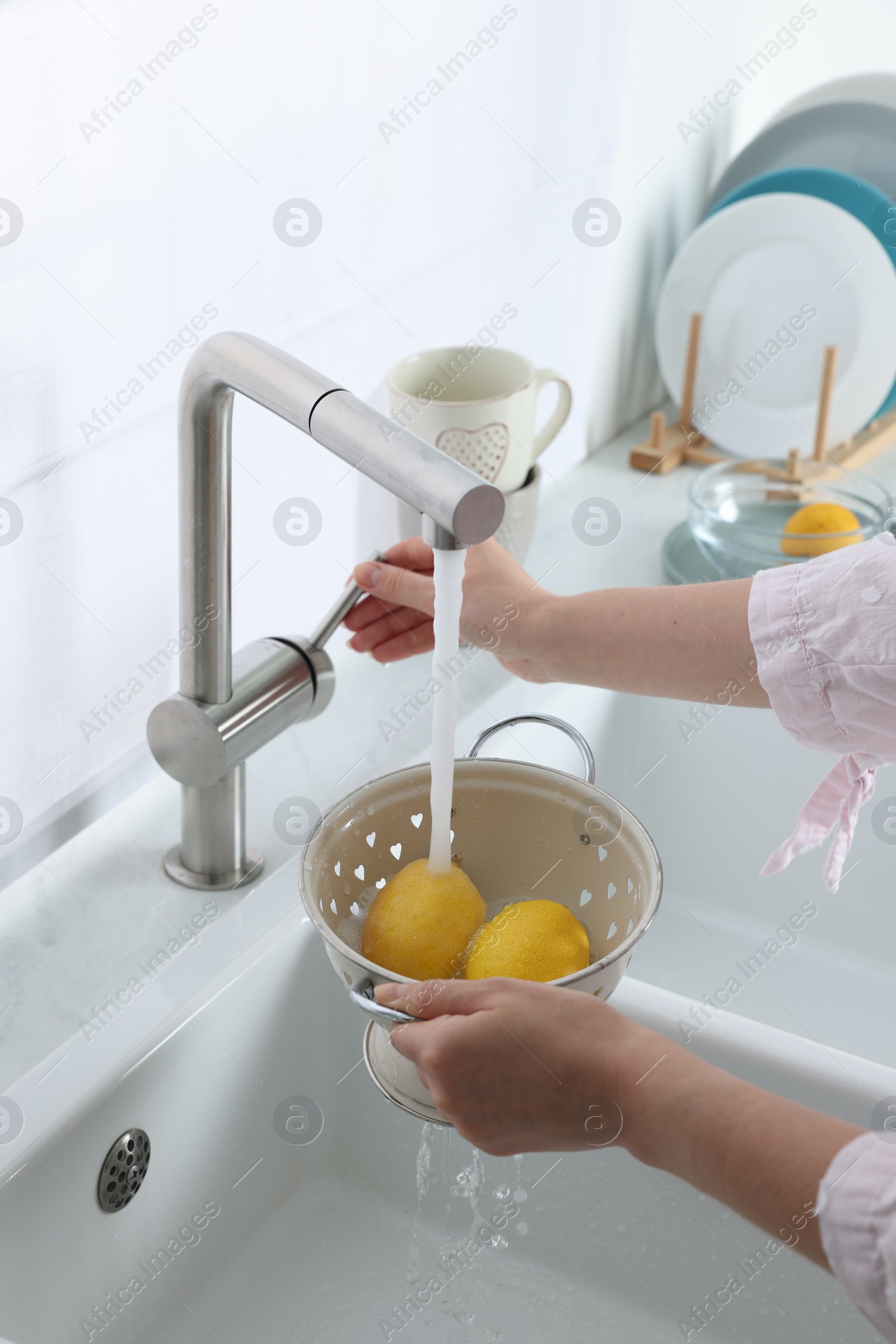 Photo of Woman washing fresh ripe lemons under tap water in kitchen, closeup