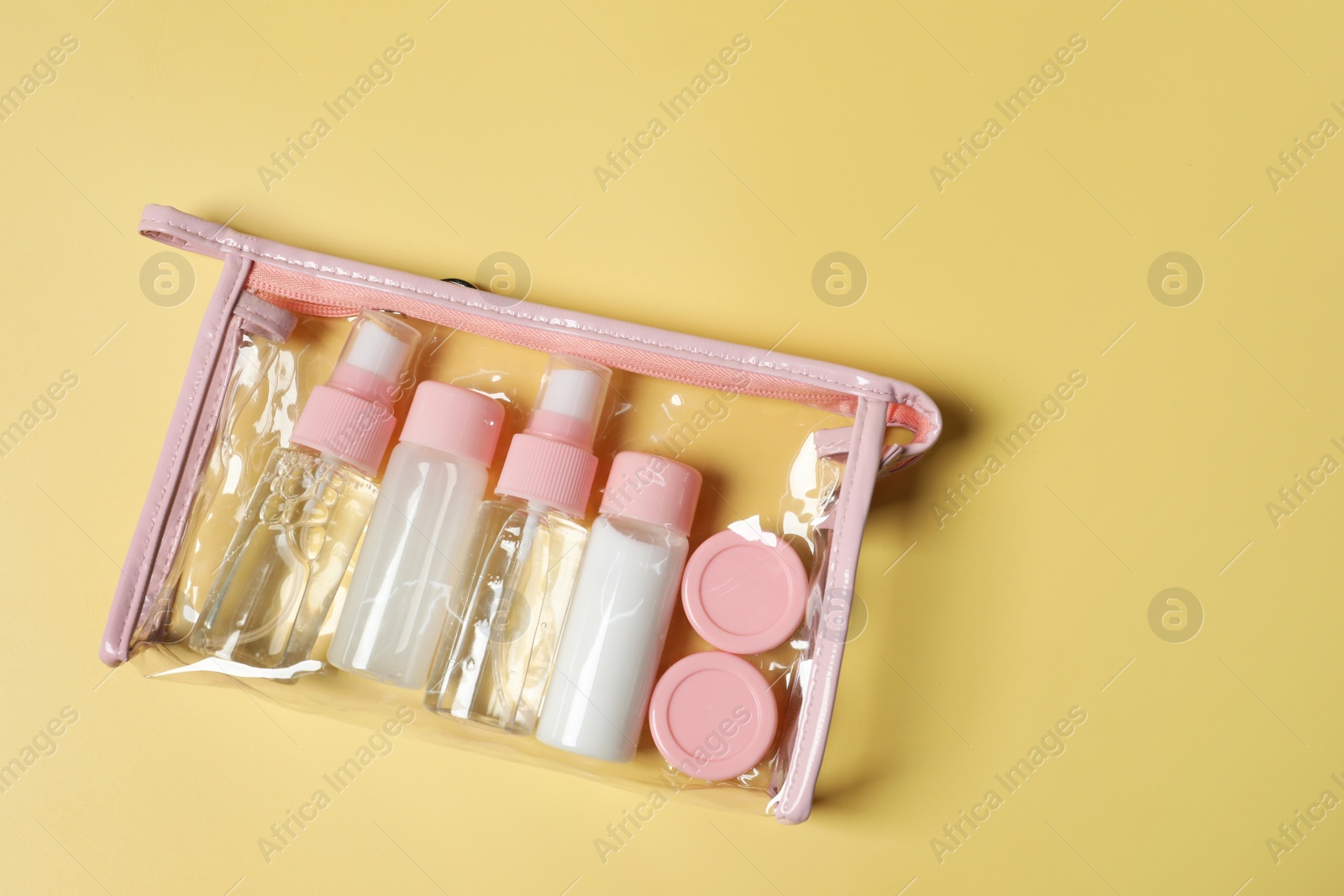 Photo of Cosmetic travel kit in plastic bag on yellow background, top view. Space for text