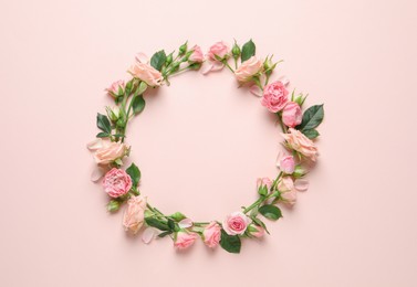 Wreath made of beautiful flowers and green leaves on pale pink background, flat lay. Space for text