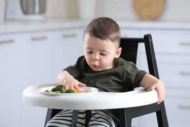 Photo of Cute little baby eating healthy food in high chair at home