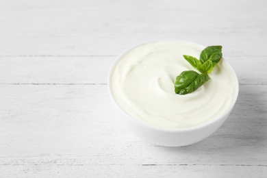 Photo of Bowl of sour cream with basil on white wooden table. Space for text