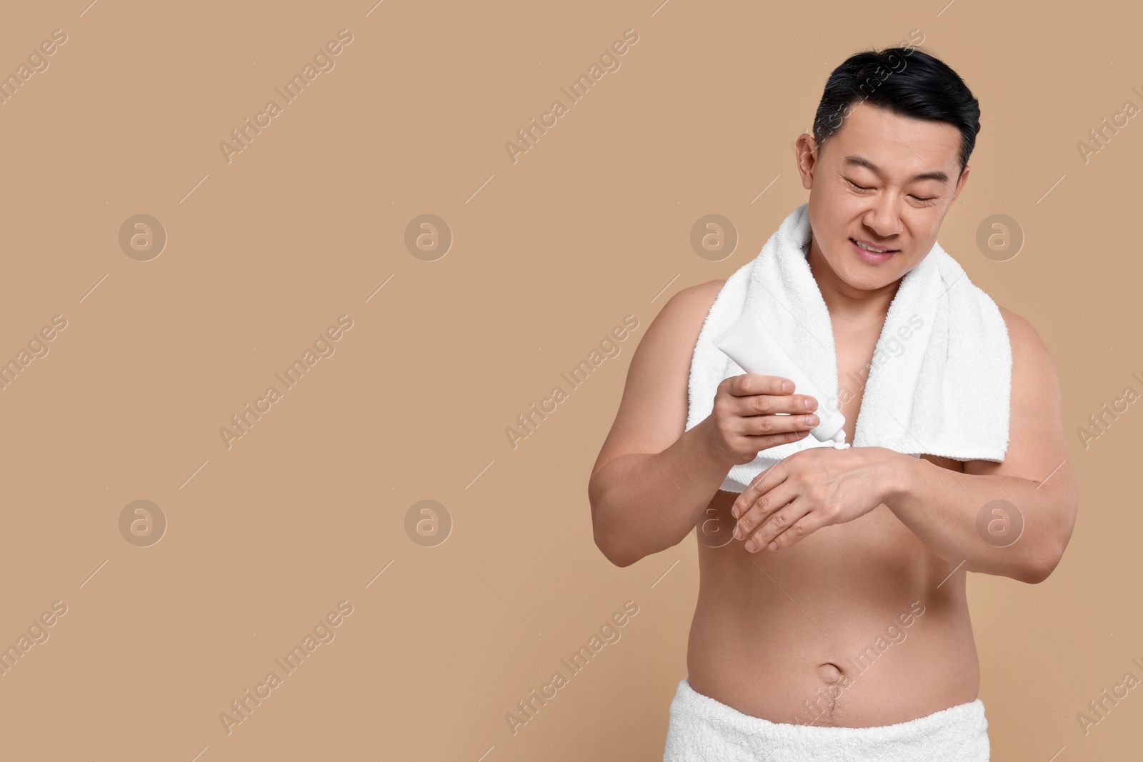 Photo of Man applying body cream onto his hand against light brown background. Space for text