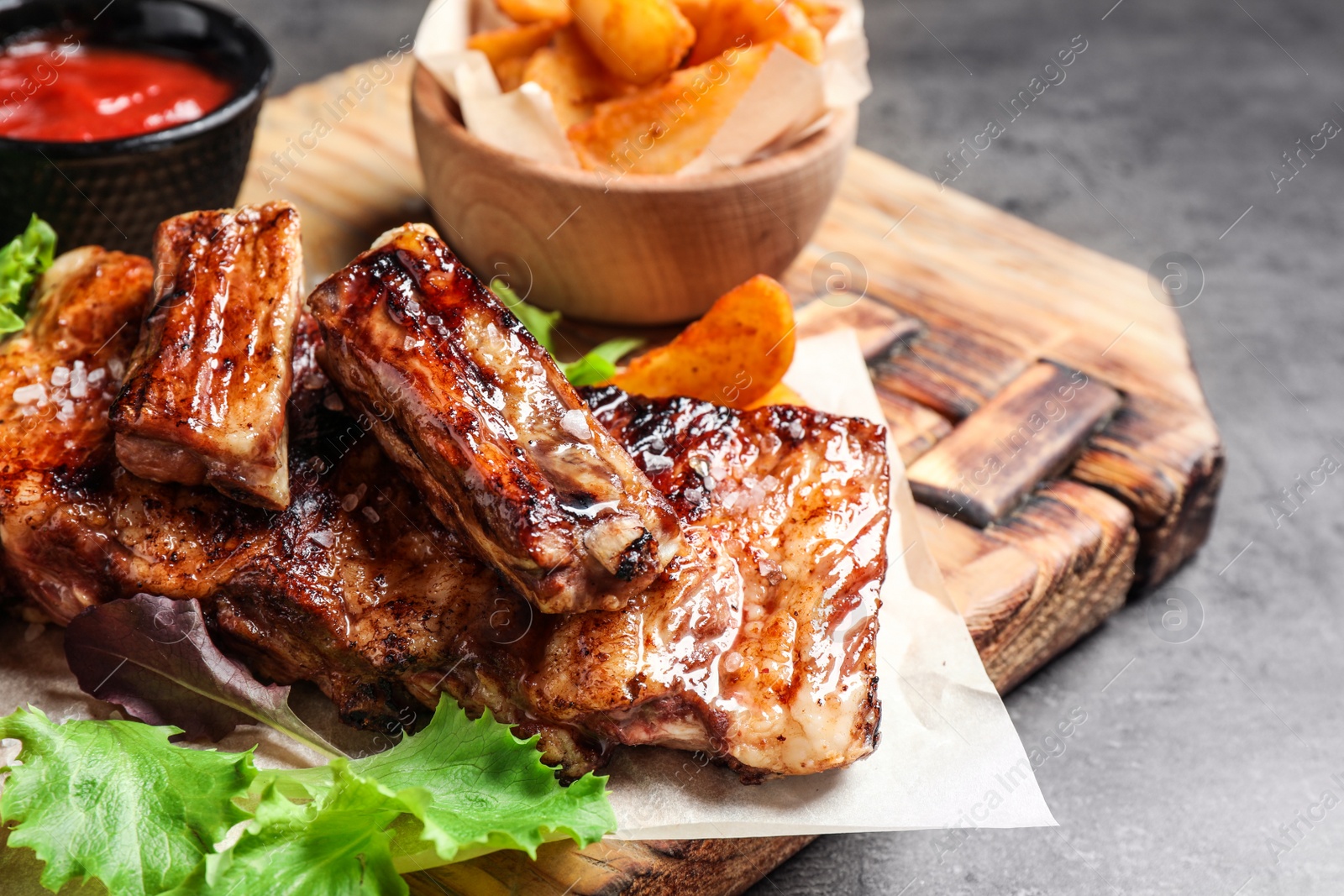 Photo of Delicious grilled ribs and garnish on grey table, closeup