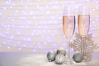 Photo of Glasses of champagne, Christmas decor and pocket watch on table against blurred lights