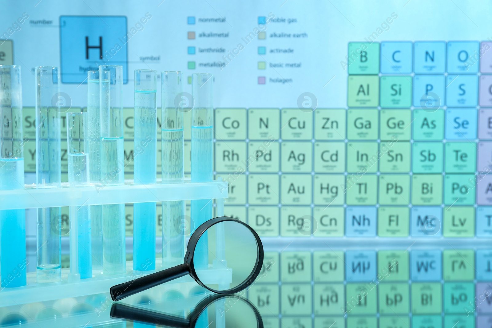 Photo of Magnifying glass and test tubes in rack on mirror surface against periodic table of chemical elements. Space for text