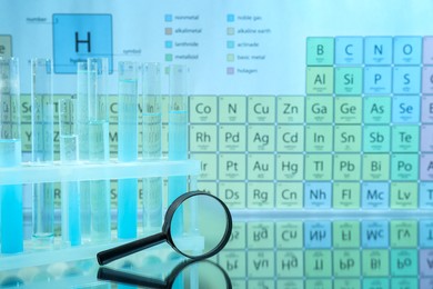 Photo of Magnifying glass and test tubes in rack on mirror surface against periodic table of chemical elements. Space for text