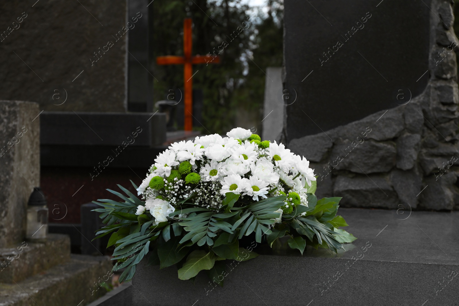 Photo of Funeral wreath of flowers on granite tombstone in cemetery