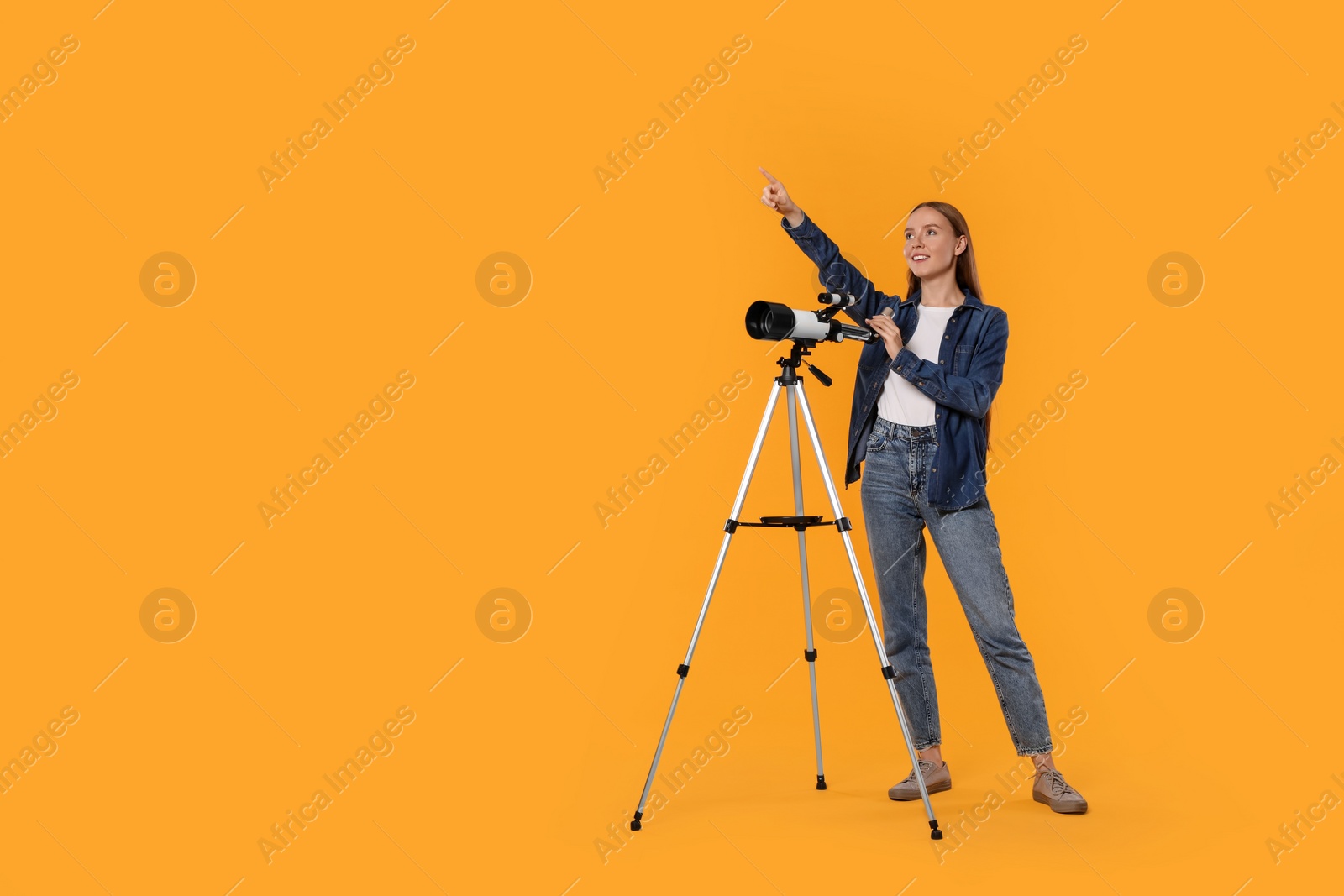 Photo of Young astronomer with telescope pointing at something on orange background, space for text