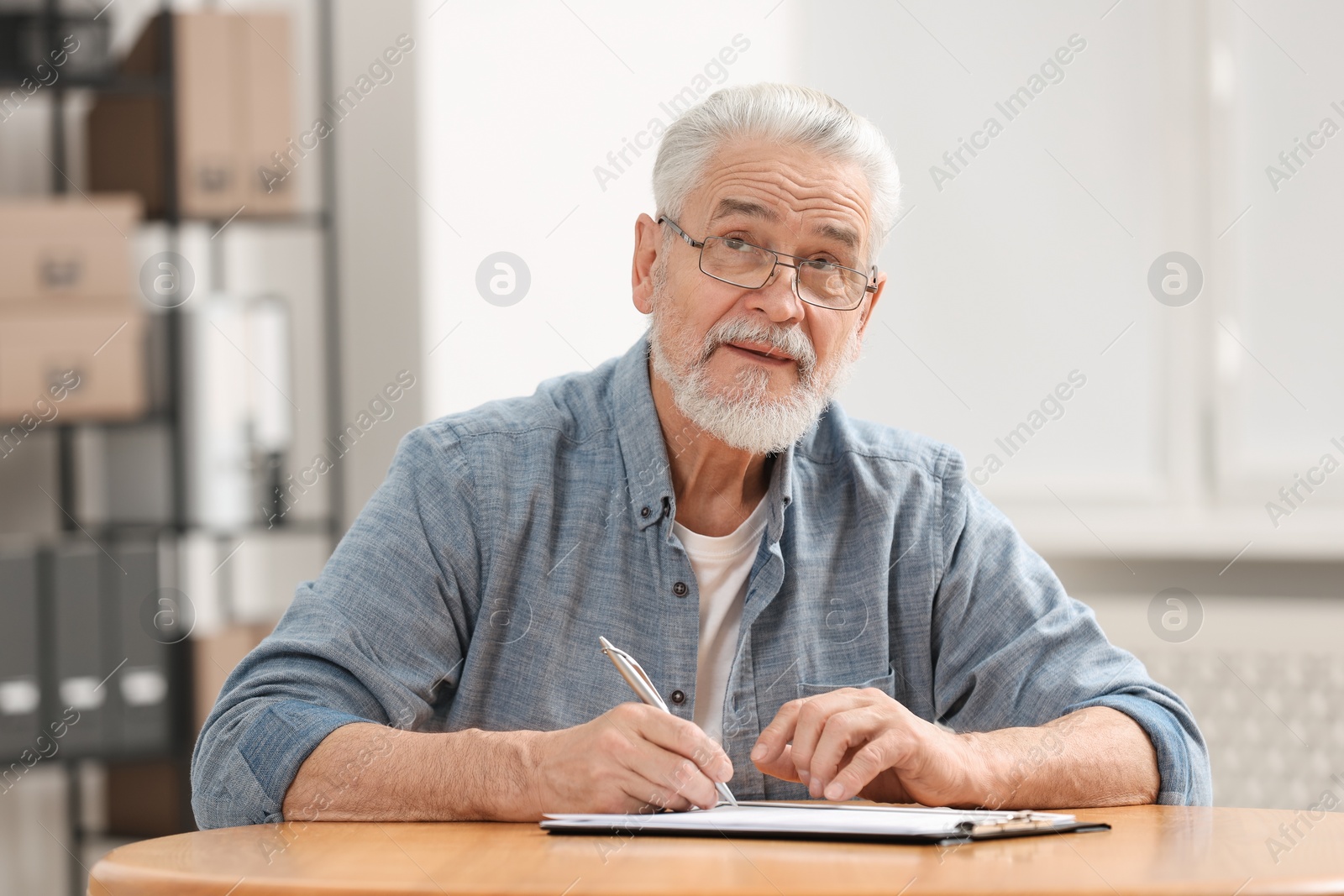 Photo of Senior man signing Last Will and Testament at table indoors