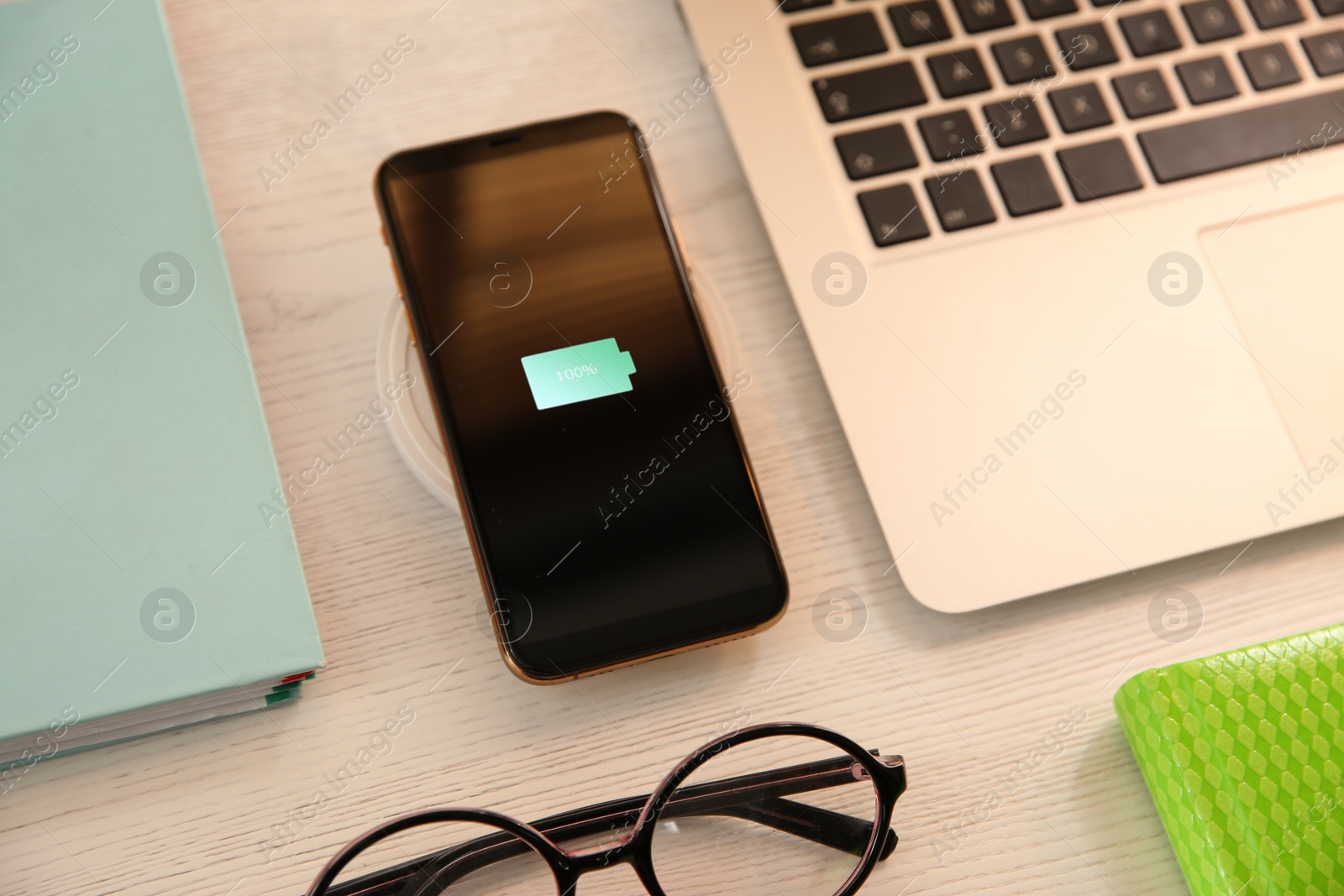 Photo of Mobile phone with wireless charger on white wooden table. Modern workplace accessory