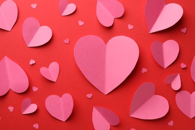 Pink paper hearts on red background, flat lay