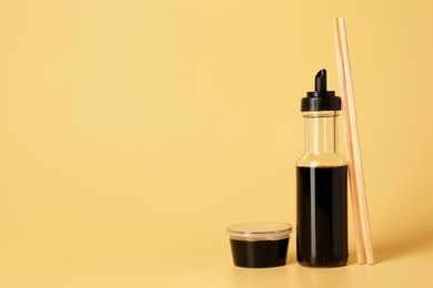 Photo of Soy sauce and chopsticks on yellow background, space for text