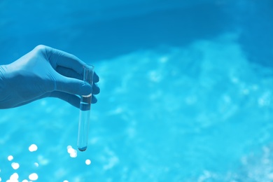 Photo of Man holding test tube with water against swimming pool on sunny day. Space for text