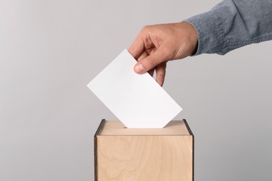 Man putting his vote into ballot box on light grey background, closeup