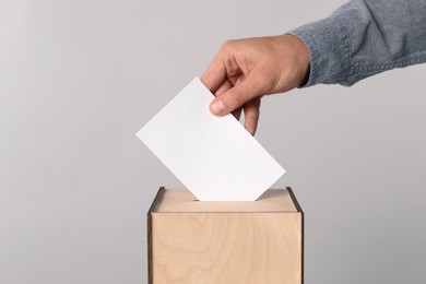 Photo of Man putting his vote into ballot box on light grey background, closeup