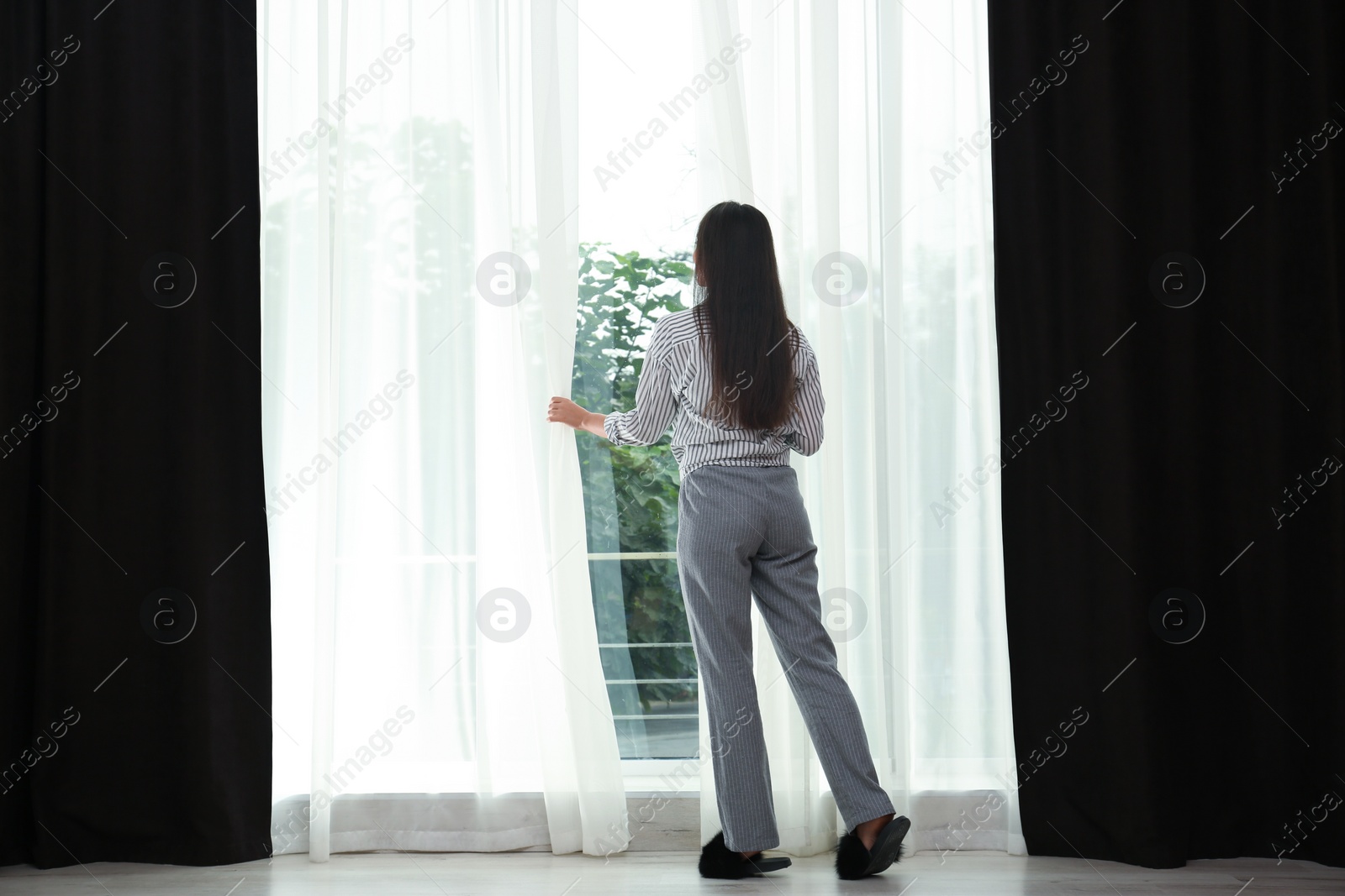 Image of Young woman opening curtains at home. Good morning