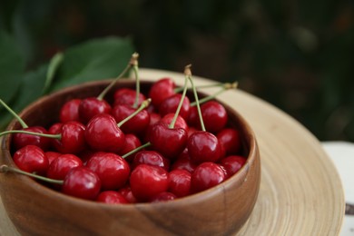 Tasty ripe red cherries in wooden bowl outdoors, closeup