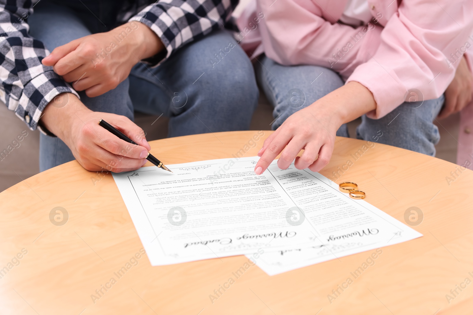 Photo of Man and woman signing marriage contract at wooden table indoors, closeup