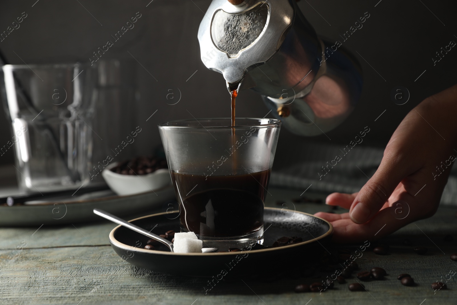 Photo of Woman pouring coffee from moka pot into glass at rustic wooden table, closeup