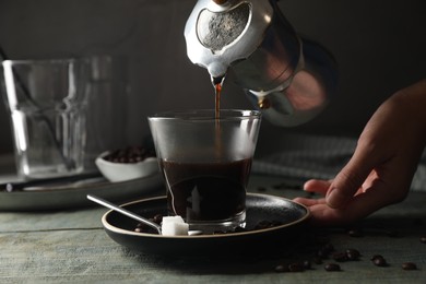 Woman pouring coffee from moka pot into glass at rustic wooden table, closeup