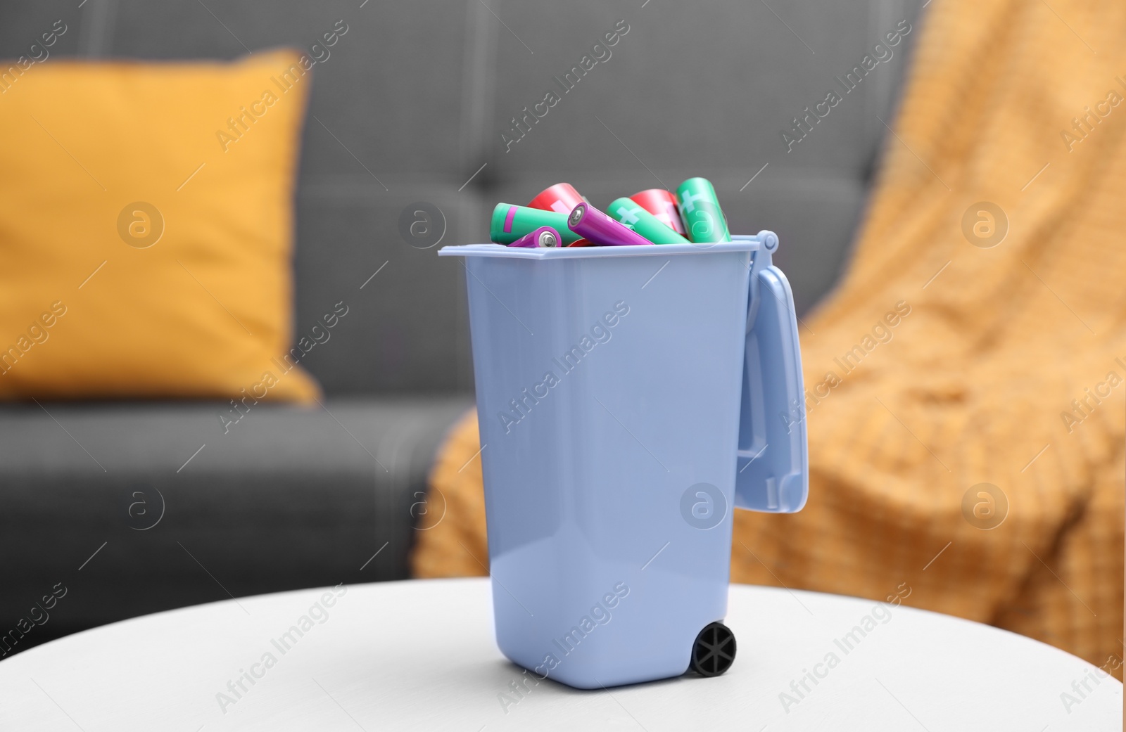 Photo of Mini recycling bin with different types of batteries on white table indoors