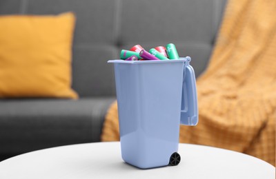 Photo of Mini recycling bin with different types of batteries on white table indoors