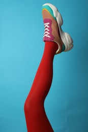 Photo of Woman wearing sneakers on light blue background, closeup