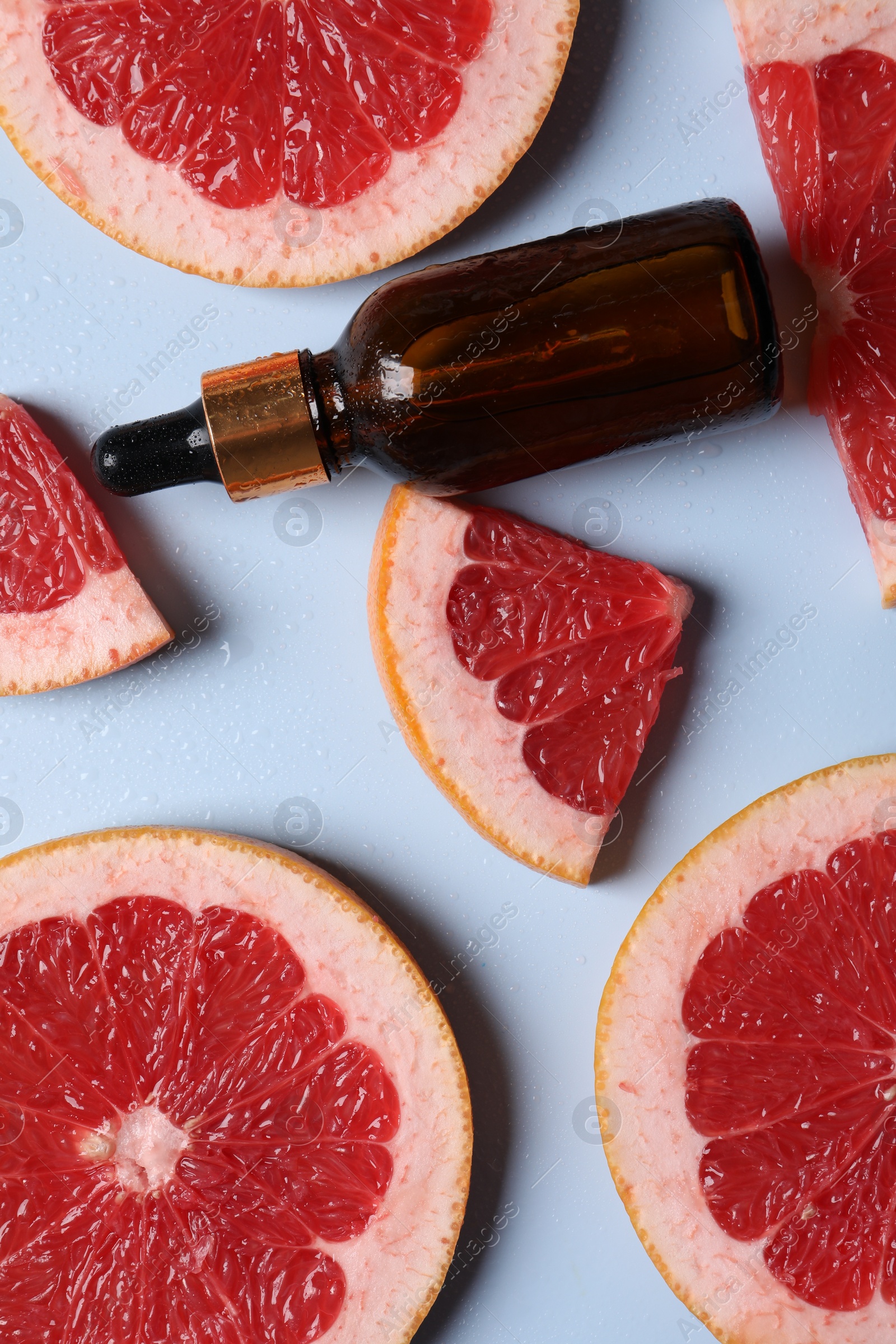 Photo of Bottle of cosmetic serum and grapefruit slices on light blue background, flat lay