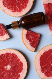 Photo of Bottle of cosmetic serum and grapefruit slices on light blue background, flat lay