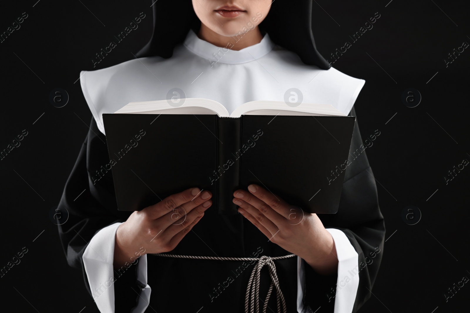 Photo of Nun reading Bible on black background, closeup