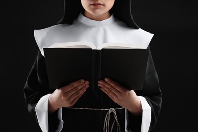 Photo of Nun reading Bible on black background, closeup