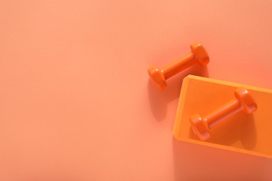 Photo of Dumbbells and yoga block on coral background, flat lay. Space for text